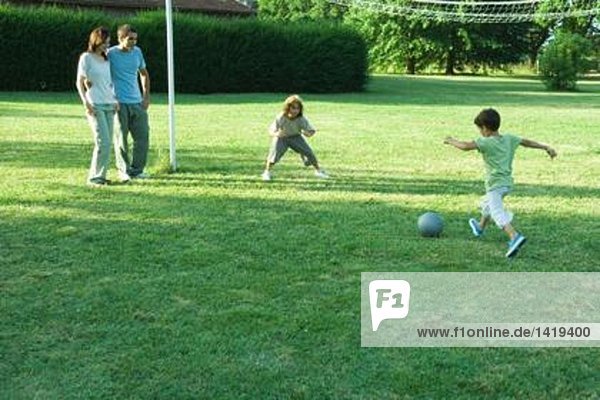 Jungen spielen Fußball  während die Eltern zusehen.