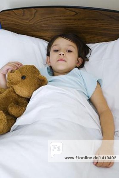 Kind im Bett liegend mit Teddybär