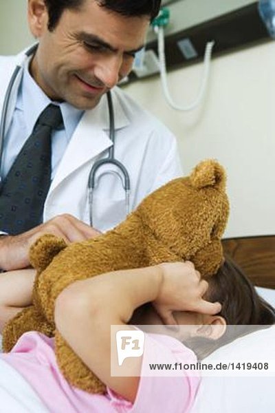 Arzt hält Teddybär bis zum Gesicht des kranken Kindes