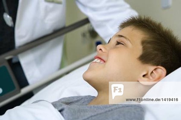 Kind im Krankenhausbett liegend  Arzt neben dem Bett stehend