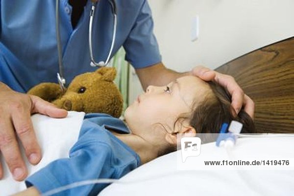 Mädchen im Krankenhausbett liegend  Krankenpflegerhand auf dem Kopf des Mädchens