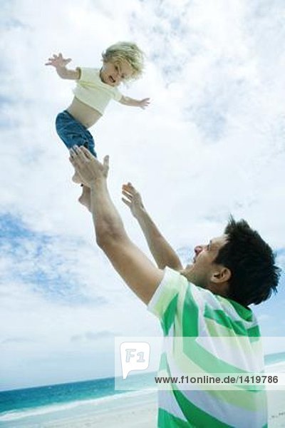Mann wirft Kind in die Luft am Strand