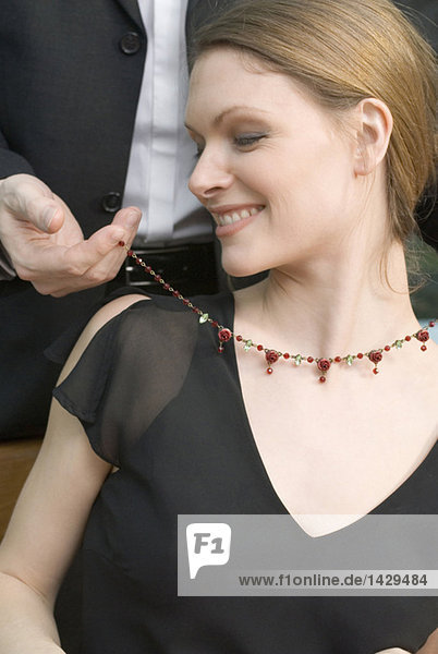 Man fastening necklace on woman's neck