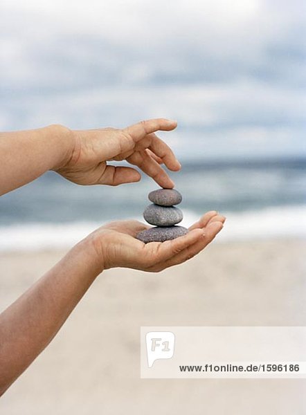 Hands holding stones with the ocean in the background.