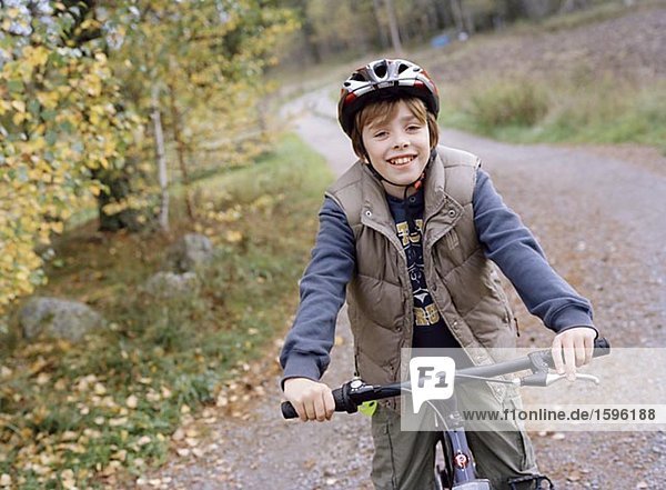 A boy bicycling on a gravel road.