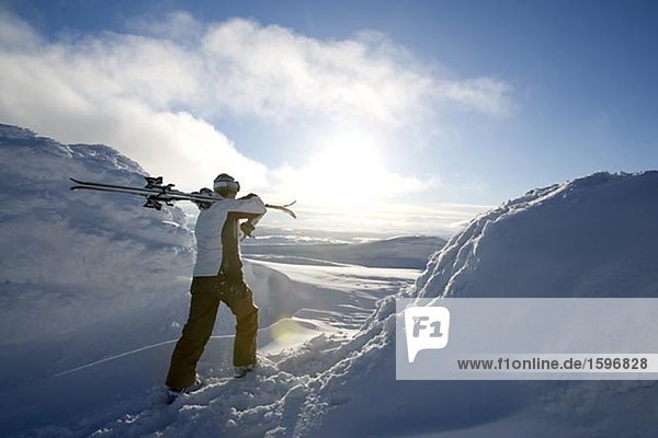 Skier carrying skies on the shoulder.