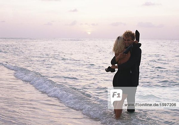 Young couple hugging at the waters edge Kuredo Maldives.