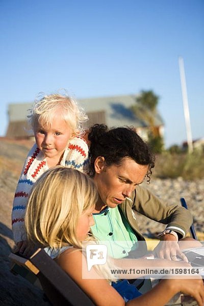 Scandinavian woman reading a newspaper her daughters sitting beside her Oland Sweden.