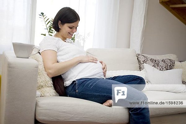 A pregnant woman sitting in a sofa Sweden.