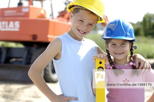 Portrait von Mädchen und jungen  Bauarbeiterhelm tragen und lächelnd