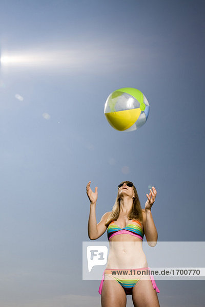 Young woman wearing bikini  throwing beach ball