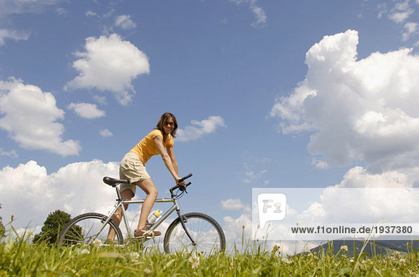 Young woman riding bicycle in meadow  side view