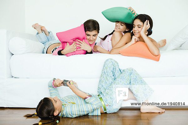 Drei junge Freundinnen liegend  die Kissen halten  während die vierte Freundin fotografiert.