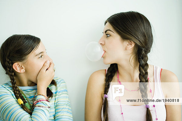 Zwei junge Freundinnen  eine bläst Blase  während die andere den Mund bedeckt.