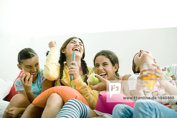 Junge Freundinnen sitzen nebeneinander  eine singt in die Fernbedienung und andere lachen.