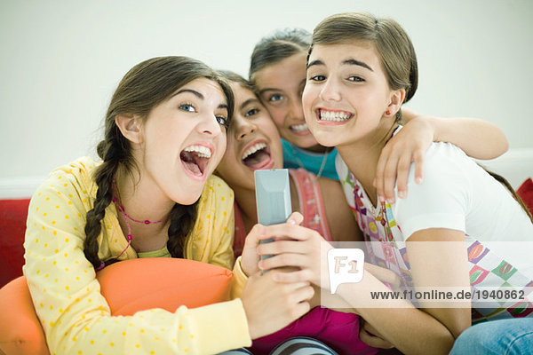 Young female friends sitting together  singing into remote control