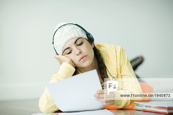 Junge Frau liegt auf dem Boden und hört Kopfhörer und macht Hausaufgaben.