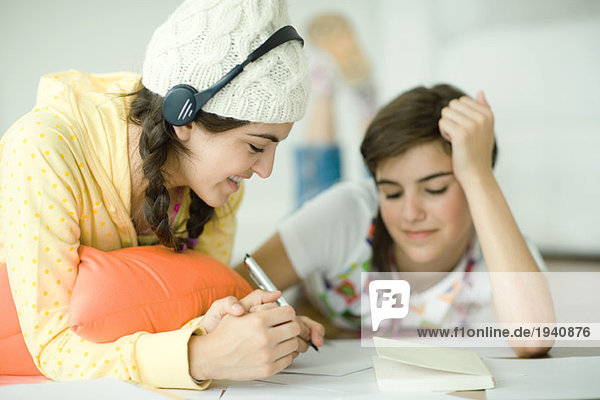 Zwei junge Freundinnen liegen auf dem Boden und machen zusammen Hausaufgaben.