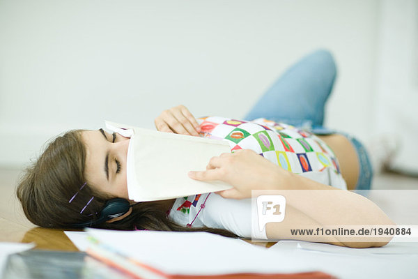 Teen girl lying on floor  doing homework  eyes closed and book over lower face