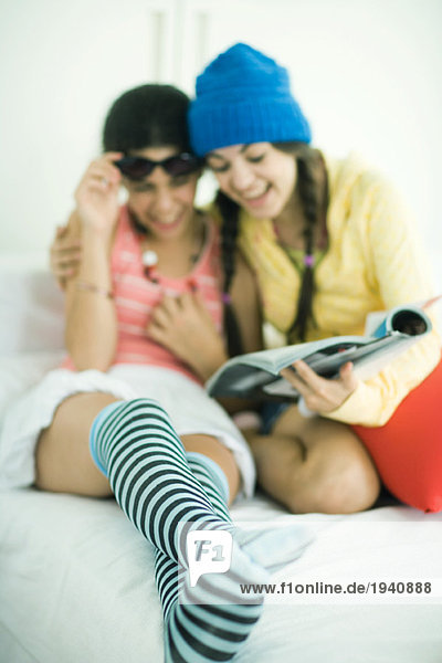 Zwei junge Freundinnen  die zusammen im Magazin suchen  lachend