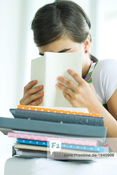 Teenagerin mit Hausaufgabenstapel  verstecktes Gesicht hinter Buch  Porträt