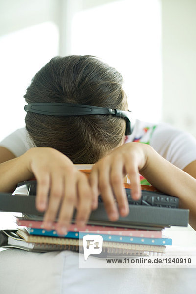Teen girl resting head on stack of homework