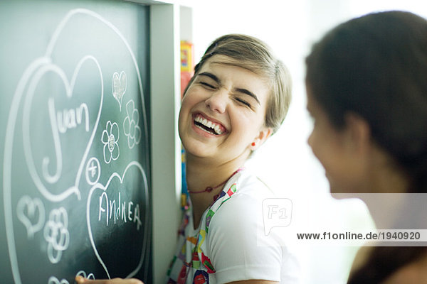 Young female friends writing names in hearts on chalkboard  laughing