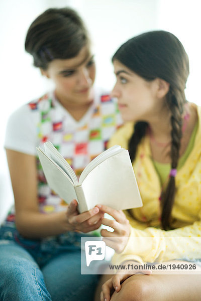 Young female friends reading book together  looking at each other
