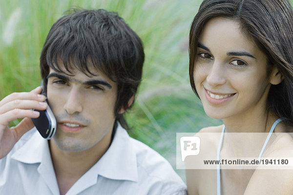 Junges Paar  Frau mit Blick auf die Kamera  Mann mit Handy  Kopf und Schultern  Porträt
