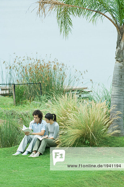 Paar auf Rasen sitzend  Bücher lesend