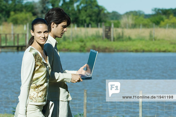Mann und Frau stehen am See  Mann hält Laptop  Frau schaut in die Kamera