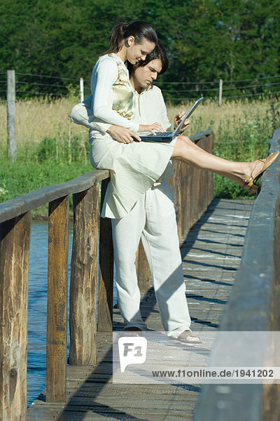Paar auf Steg über Wasser  Frau auf Schiene sitzend  mit Laptop