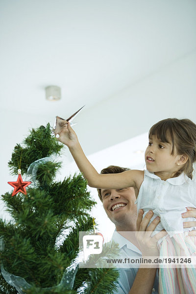 Mann hebt Mädchen  um Stern auf den Weihnachtsbaum zu setzen
