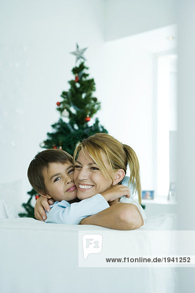Junge und Mutter auf dem Sofa umarmen sich  Weihnachtsbaum im Hintergrund