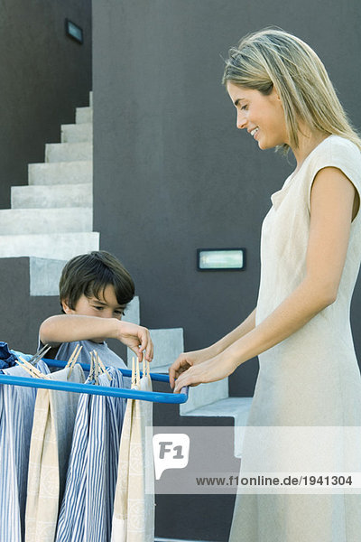 Kleiner Junge hilft Mutter beim Aufhängen der Wäsche am Trockengestell