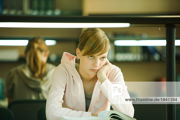 Junge Frau studiert in der Universitätsbibliothek  hält Kopf  schaut weg