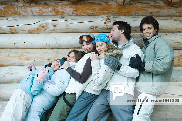 Group in winter clothes falling back onto each other  three quarter length  in front of log wall  portrait