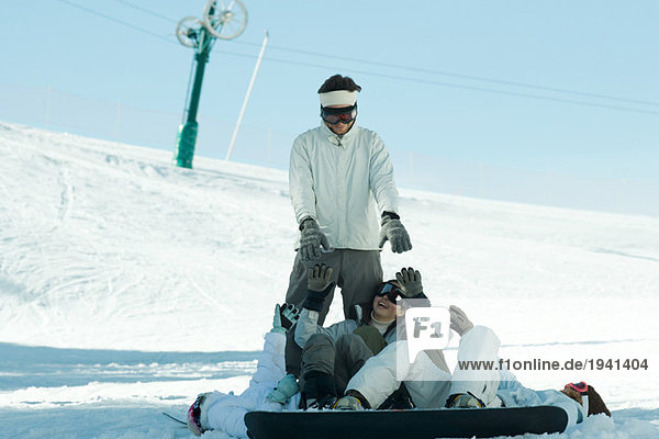 Young snowboarders lying on ground reaching for young man standing behind them