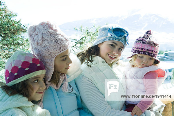 Drei Teenager- oder Kindermädchen mit Kleinkind in den Bergen  alle mit Wintermänteln und Hüten  Portrait