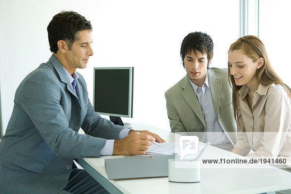 Young couple sitting across desk from businessman  businessman pointing to document