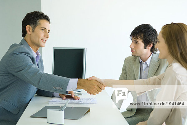 Young couple sitting across desk from businessman  woman shaking hands with businessman  side view