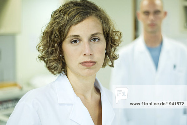 Female doctor looking at camera  male colleague in background  portrait