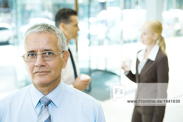 Erwachsener Geschäftsmann mit Blick auf Kamera  Portrait  Mitarbeiter im Hintergrund