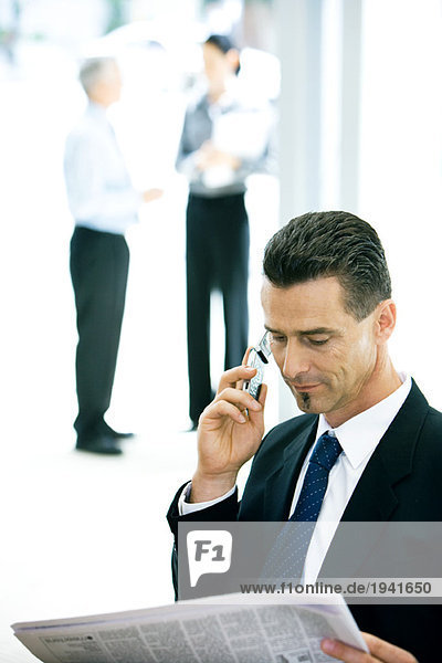 Businessman using cell phone  looking at newspaper
