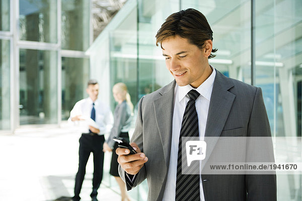 Junger Geschäftsmann schaut auf Handy  lächelnd  Portrait