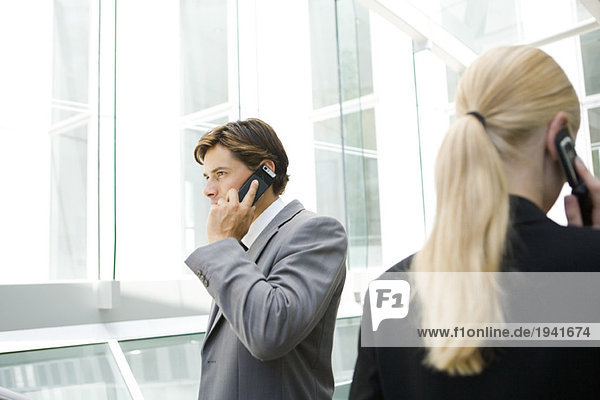 Two business associates walking past each other by window  both using cell phones