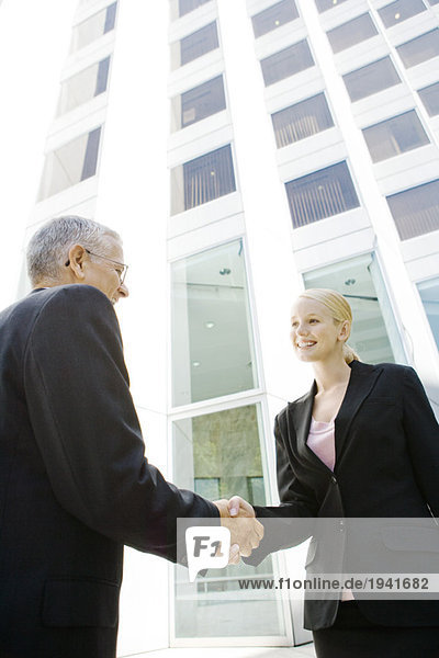 Two business associates shaking hands  smiling  building in background