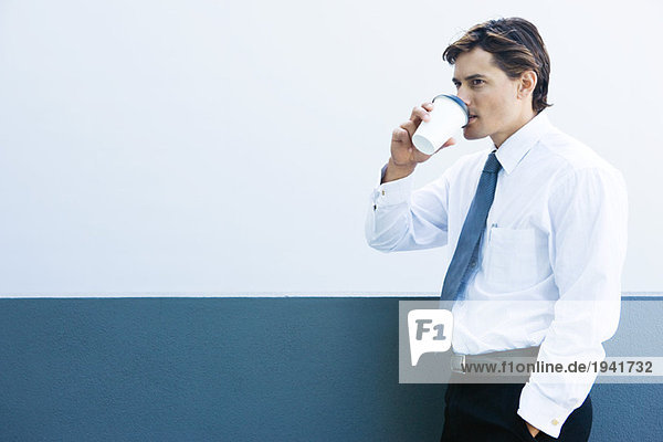 Junger Geschäftsmann trinkt Heißgetränk  Hand in Tasche  Seitenansicht