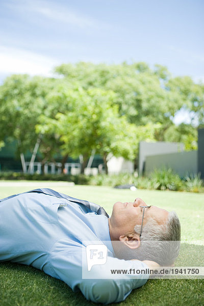 Mature businessman lying on ground outdoors  hands behind head  eyes closed