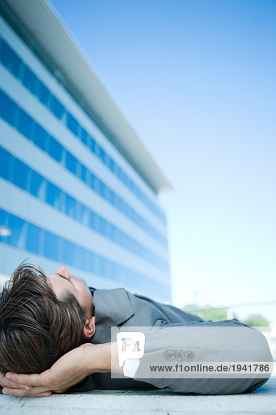 Businessman lying on ground outdoors  hands behind head  cropped view